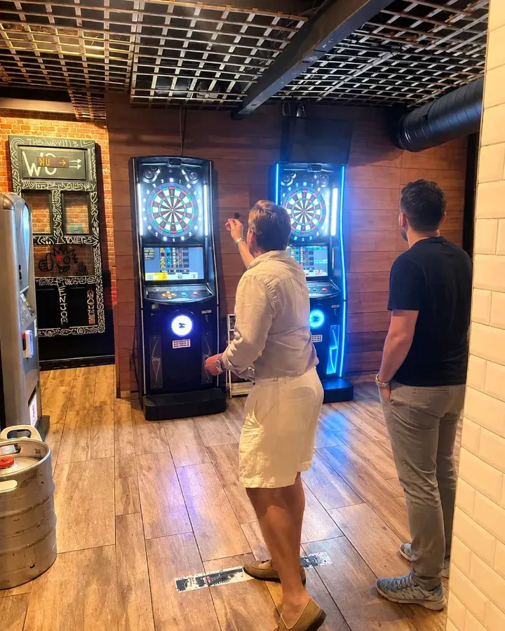 Dos clientes jugando a los dardos en las máquinas iluminadas de De Locos