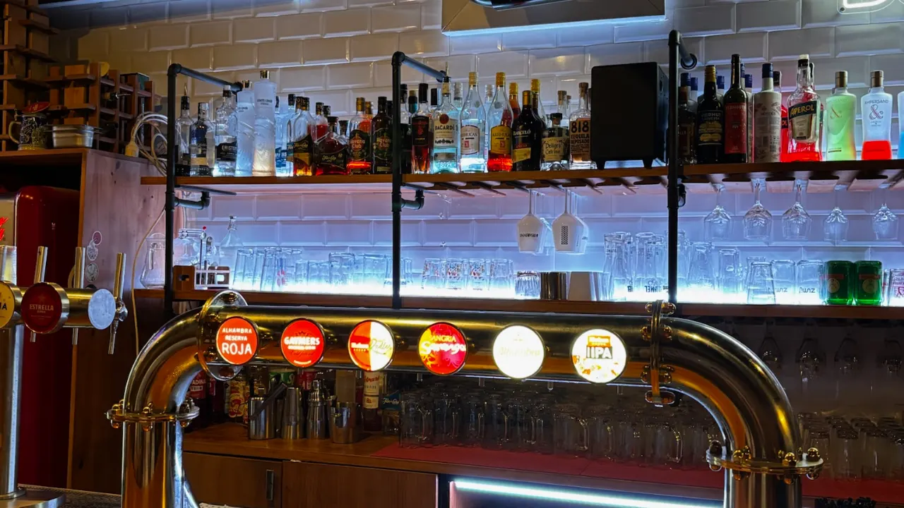 Grifo de cerveza de barril con varias marcas y botellas iluminadas en la barra de De Locos