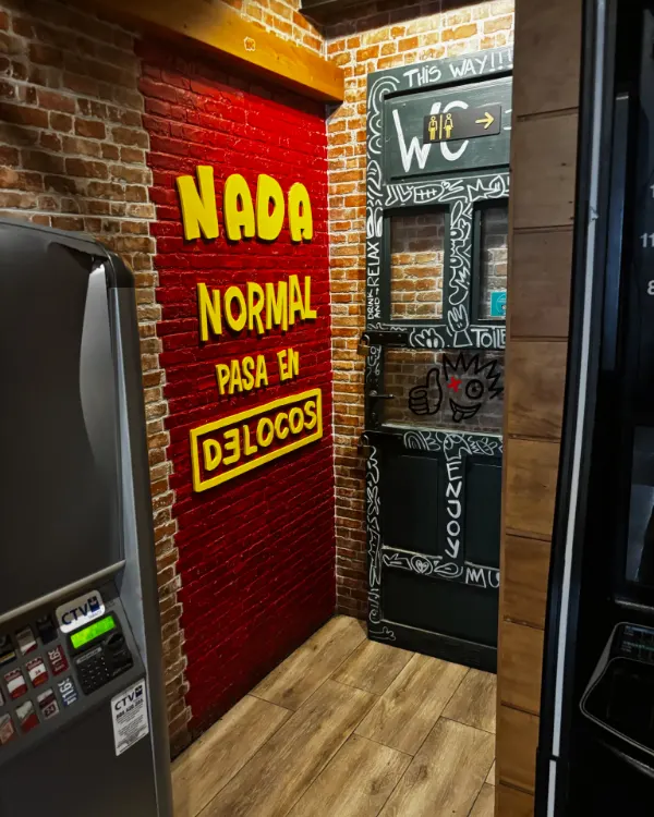 Pared de ladrillo rojo con el mensaje «Nada normal pasa en De Locos»